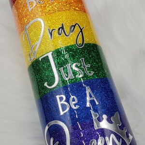 May include: A rainbow glitter tumbler with the text "Don't Be A Drag Just Be A Queen" in silver lettering. The tumbler has a crown graphic on the bottom.