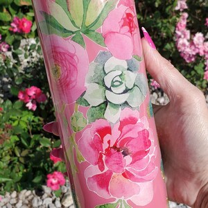 Peut inclure: Un gobelet cylindrique rose orné d'un motif floral et de plantes succulentes de style aquarelle dans des tons de rose et de vert, agrémenté de taches de paillettes dorées et turquoise, avec le logo The Glittery Bohemian inscrit en bas.