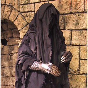 Può includere: Una figura oscura in un mantello nero con cappuccio e bordi strappati, in piedi contro un muro di pietra. Il costume presenta un'armatura metallica per le mani. L'estetica generale suggerisce un tema fantasy o gotico.