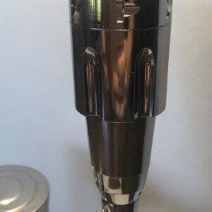 K&ouml;nnte beinhalten: Ein schwarzer und verchromter Wasserhahn mit einem dekorativen, geriffelten Auslauf. Der Wasserhahn hat einen runden, verchromten Griff mit einem schwarzen Knopf.