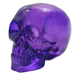 May include: A purple glass skull figurine. The skull is detailed with eye sockets, a nose, and teeth.