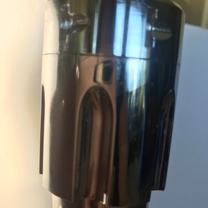 K&ouml;nnte beinhalten: Nahaufnahme eines verchromten Metall-Wasserhahn-Griffs mit strukturiertem Design. Der Griff hat zwei kleine Schrauben oben.