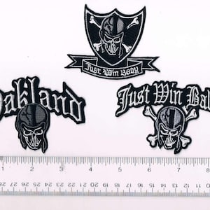 May include: Three black and white embroidered patches with the Oakland Raiders logo. The patches feature a skull and crossbones with the words "Oakland", "Just Win Baby", and "Just Win Baby" in a gothic font.