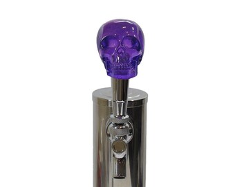 May include: Purple glass skull beer tap handle. The skull is translucent and has a detailed design. The tap handle is attached to a silver metal tap.