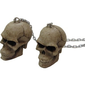 May include: Two small, detailed, beige skull figurines connected by a silver chain. The skulls have a realistic appearance with visible teeth and eye sockets.