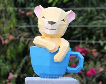 May include: A yellow papercraft lion figurine sitting in a blue ceramic teacup. The cup is on a gray fabric surface.