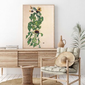 May include: A framed print of a watercolor painting of a sunflower plant with green leaves and yellow petals. The painting is on a cream background.