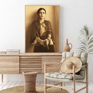 May include: A black and white photograph of a woman holding a gun. She is wearing a dark robe and a necklace. The background is a light wood panel.