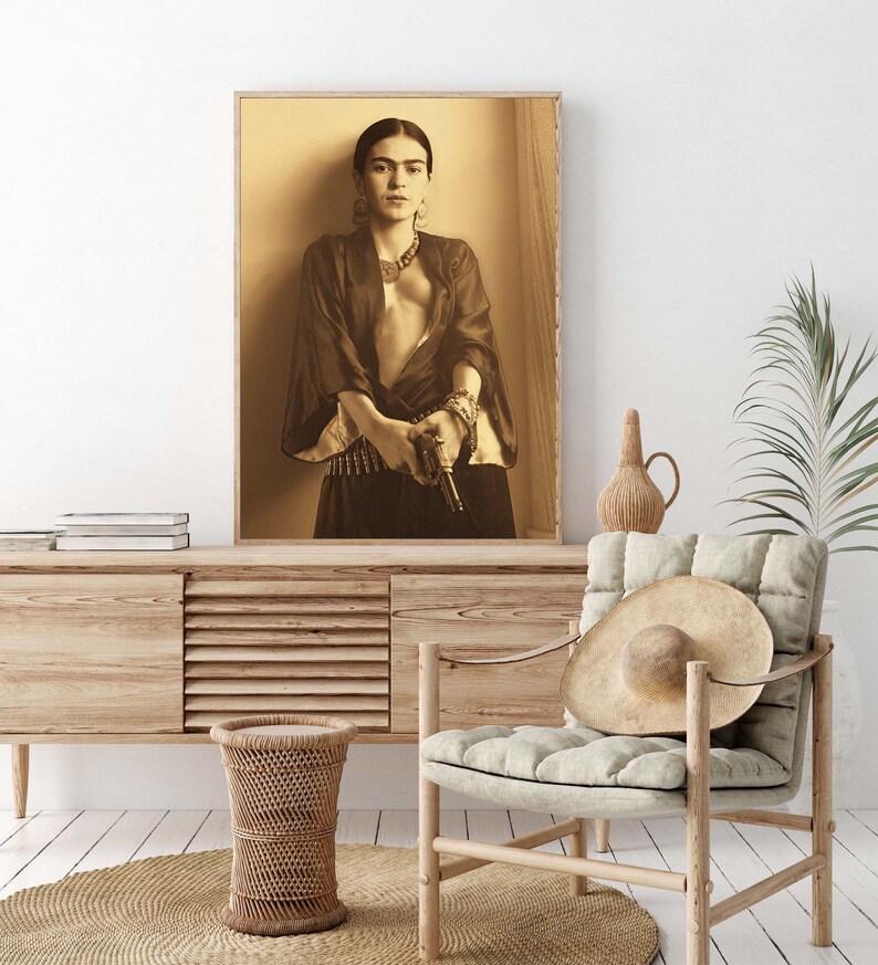 May include: A black and white photograph of a woman holding a gun. She is wearing a dark robe and a necklace. The background is a light wood panel.