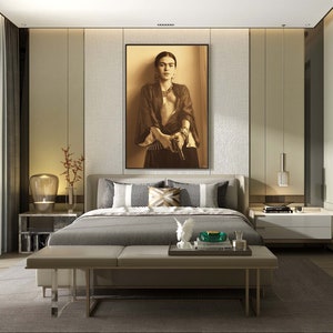 May include: A modern bedroom with a large bed, a bench at the foot of the bed, and a framed picture of Frida Kahlo on the wall. The bed has a gray headboard and a gray comforter. The bench is upholstered in a light brown fabric. The picture is in a black frame and features a sepia-toned image of Frida Kahlo holding a gun.