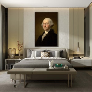 May include: A bedroom interior with a large framed portrait of George Washington hanging above a gray upholstered bed with white and brown patterned pillows. The bed is positioned in front of a wall with a textured beige wallpaper. There is a white nightstand on each side of the bed with a lamp on each nightstand. A white bench sits in front of the bed. The room has a large window with white curtains and a gray rug on the floor.