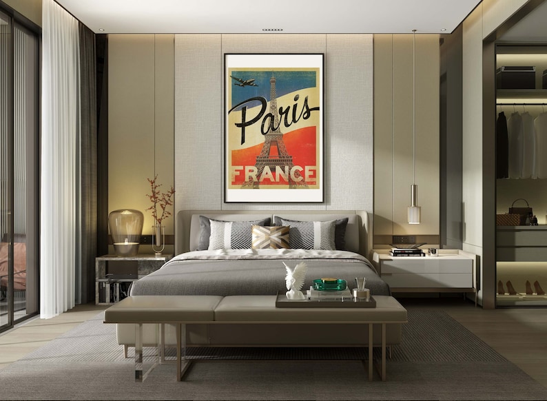 Op de afbeelding: Een slaapkamerinterieur met een grijs bed, een grijze bank en een ingelijste poster met de tekst "Paris France" en een afbeelding van de Eiffeltoren. De poster hangt aan een muur met een textuur.