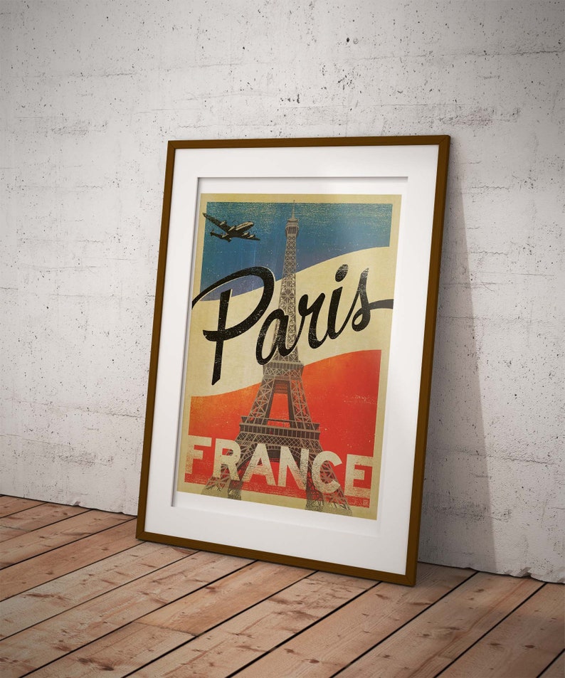 Op de afbeelding: Een vintage poster met een bruin frame met daarop de Eiffeltoren in Parijs, Frankrijk. De poster heeft een blauw, wit en rood kleurenschema en de tekst "Paris France" is in zwart gedrukt.