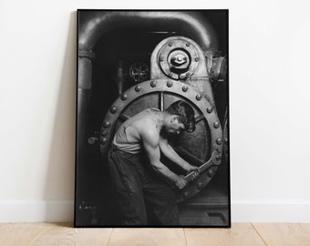 May include: A black and white photograph of a man working on a large industrial machine. He is wearing a work shirt and is using a wrench to tighten a bolt.