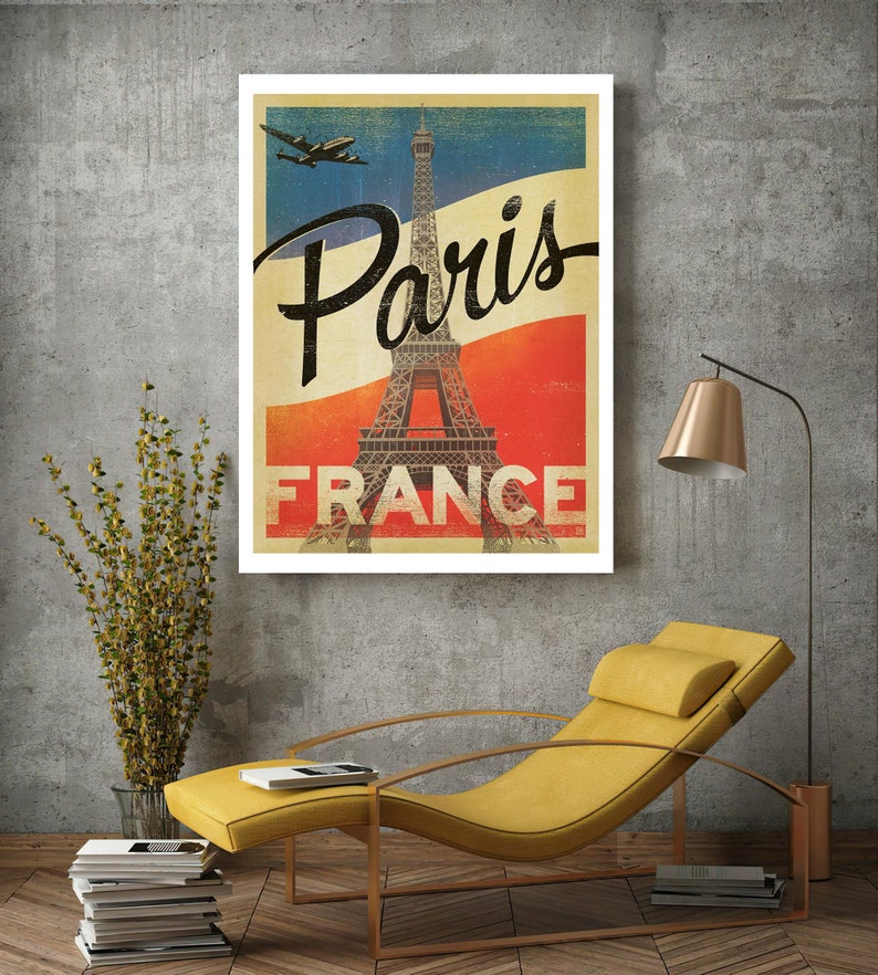 Op de afbeelding: Vintage reisposter met de Eiffeltoren in Parijs, Frankrijk. De poster heeft een rood-wit-blauw kleurenschema met een vliegtuig dat erboven vliegt. De tekst "Paris France" is in zwart gedrukt.