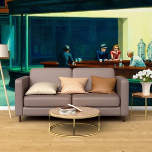 May include: A painting of a diner scene with four people sitting at the counter. The painting is on a wall behind a brown couch, a coffee table, and a side table with a vase of white flowers.