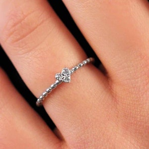 Woman wearing tiny heart diamond ring with beaded band, minimalist gold stackable ring styled on hand with yellow gold