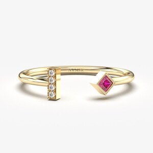 May include: A gold ring featuring a vertical bar of small diamonds and a square ruby set in a gold frame. The ring is open on one side.