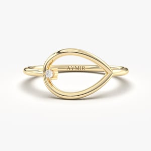 May include: A gold ring with a teardrop-shaped design. A small, clear gemstone is set near the top of the teardrop. The ring is on a white background. The word "AYMIR" is engraved on the ring.