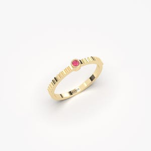Pu&ograve; includere: Un anello d'oro con una piccola gemma rosa e rotonda. La fascia dell'anello presenta un design strutturato e scanalato. L'anello &egrave; posto su uno sfondo bianco. Il nome del marchio "AYMIR" &egrave; inciso sull'anello.