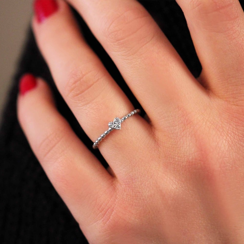 Woman wearing tiny heart diamond ring with beaded band, minimalist gold stackable ring styled on hand with yellow gold