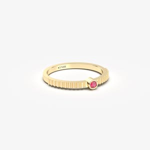 Pu&ograve; includere: Un anello d'oro con una fascia strutturata e una piccola gemma rosa rotonda. L'anello ha un design minimalista con una singola gemma incastonata in una lunetta. L'anello &egrave; taglia 14.