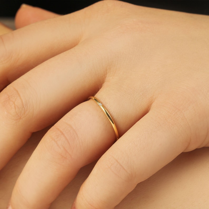 Woman wearing single diamond minimalist ring, 8K gold delicate solitaire ring styled on hand with yellow gold