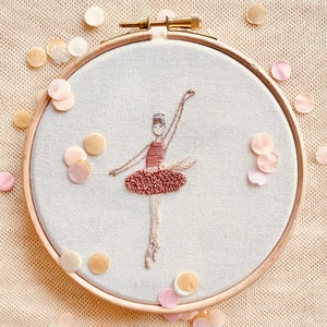 May include: A hand-stitched embroidery hoop featuring a ballerina in a pink dress. The hoop is surrounded by confetti.