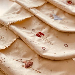 以下が含まれることがあります： クリーム色のクリスマスストッキング。バレエダンサーと雪の結晶が刺繍されています。各ストッキングはスカラップエッジと赤、茶色、青の色合いの繊細な刺繍が特徴です。お祝いのホリデーデコレーション。