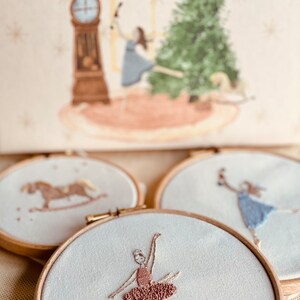 May include: Three embroidered hoop art pieces with a white background. One hoop features a rocking horse, another features a ballerina in a pink tutu, and the last hoop features a ballerina in a blue dress.