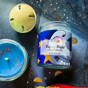 May include: A blue soy blend candle with a white moon and stars design. The label reads "Nighty Night Bedtime & Punishment" and "Pretty Witch Craft".