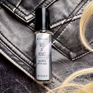 May include: A small, clear glass bottle with a black rollerball top. The bottle is labelled "Pretty Witch Craft" and "Wild at Heart" with the text "Full Moons Guitar Solos" and "10ml Perfume Oil".