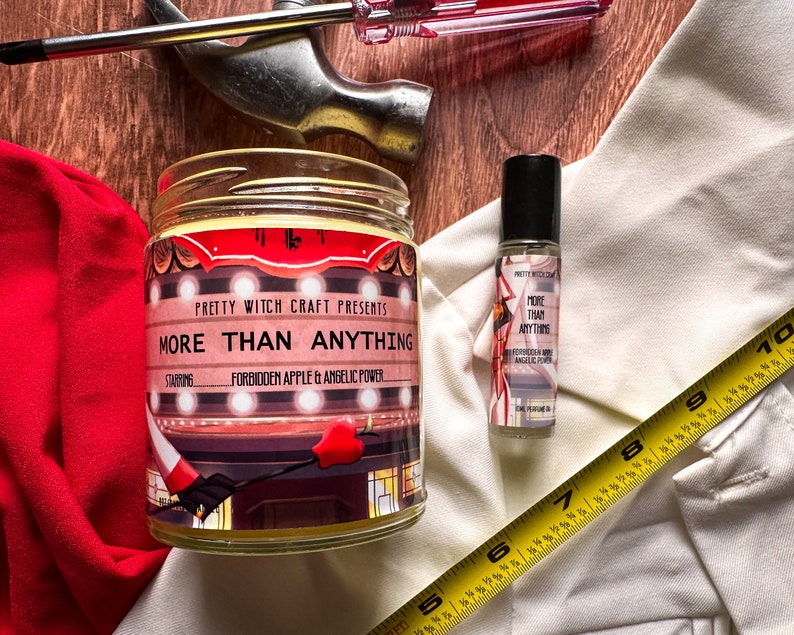 May include: A candle and a roll-on bottle of essential oil with the text "More Than Anything" on both. The candle is in a glass jar with a red and white label. The essential oil is in a clear glass bottle with a black cap. The candle is labelled "Forbidden Apple & Angelic Power".