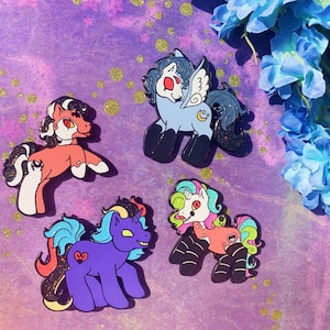 Puede incluir: Cuatro pines de esmalte con caballos de dibujos animados de diferentes colores y diseños. Los caballos están todos en posición de pie con las patas extendidas. Los pines están sobre un fondo morado con purpurina.