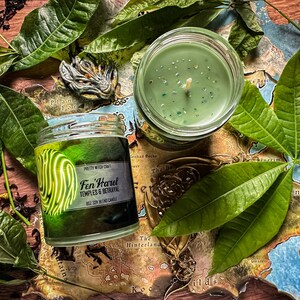May include: A green soy blend candle in a glass jar with a label that reads "Fen'Harel Temples & Betrayal". The candle is surrounded by green leaves and a map.
