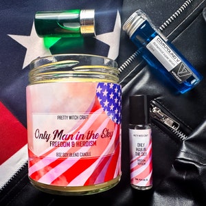 May include: A candle with a red, white, and blue American flag design. The candle is labeled "Only Man in the Sky" and "Freedom & Heroism". The candle is surrounded by other products, including a small bottle of perfume oil, a green glass bottle, and a blue glass bottle.