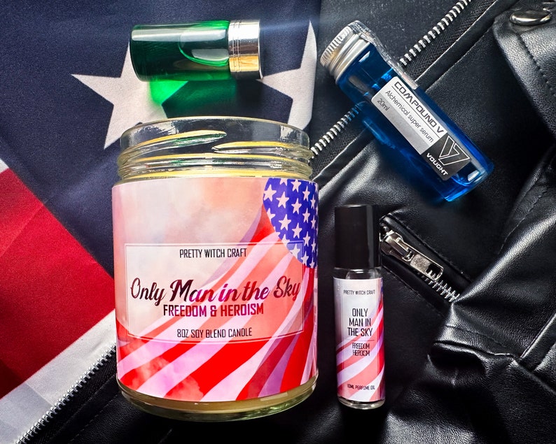 May include: A candle with a red, white, and blue American flag design. The candle is labeled "Only Man in the Sky" and "Freedom & Heroism". The candle is surrounded by other products, including a small bottle of perfume oil, a green glass bottle, and a blue glass bottle.