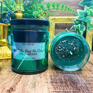 May include: A green soy blend candle with a black label that reads "Sor The Had No Choice Apples & Arrogance 8oz Soy Blend Candle". The candle is in a clear glass jar with a black lid. The candle is sitting on a wooden surface.