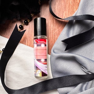 May include: A clear glass bottle with a black cap and a colorful label. The label features a pink and white design with a building and lights. The bottle is sitting on a white surface.