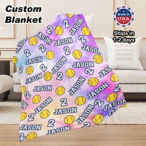 May include: A soft, white fleece blanket with a tie-dye pattern in shades of pink, purple, and blue. The blanket is decorated with a repeating pattern of yellow softball images and the name "Jason" with the number "2" printed on it.