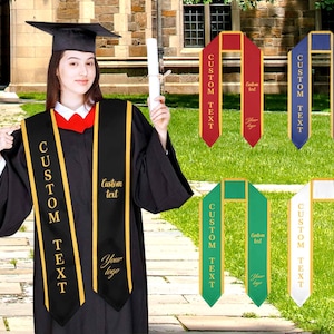 May include: A person in a black graduation gown and mortarboard, with a red collar. The gown has a custom sash with gold lettering and trim. Other sashes in red, blue, green, and white are shown, each with custom text and a logo.