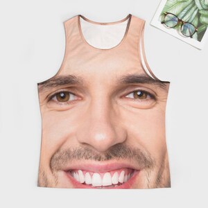 May include: A white tank top with a printed image of a man's face. The man is smiling and has brown hair and eyes.