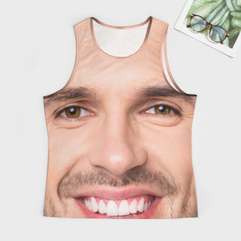 May include: A white tank top with a printed image of a man's face. The man is smiling and has brown hair and eyes.