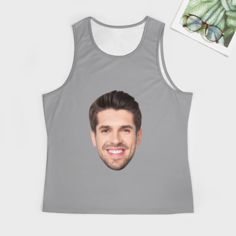 May include: A gray tank top with a white face printed on the front. The face is of a man with brown hair and a smile.
