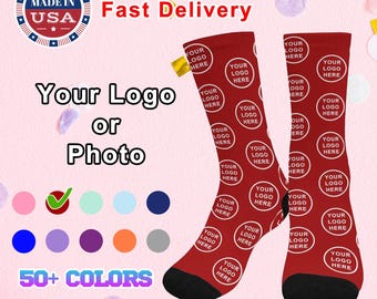 May include: Two red socks with a white circle pattern that says "Your Logo Here" on each sock. The socks are on a pink background with confetti. The text "Made in USA Fast Delivery" is at the top of the image. The text "Your Logo or Photo" is in the middle of the image. There is a checkmark next to a row of coloured circles and the text "50+ COLORS" at the bottom of the image.