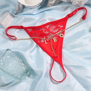 May include: Red lace lingerie with a gold chain and charm accents spelling "LOVE".