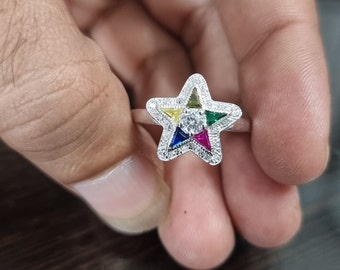 May include: A silver ring with a five-pointed star design. The star is set with a clear center stone and five smaller colored stones in a rainbow pattern.