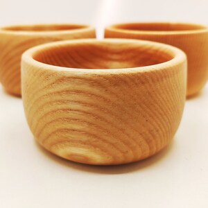 Peut inclure: Trois bols en bois, chacun avec un motif de grain unique, sont disposés sur une surface blanche. Les bols sont en bois naturel et ont une forme ronde et lisse.