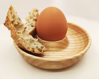Puede incluir: Un huevo marrón en un huevo de madera con un trozo de pan al lado.