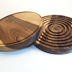 Puede incluir: Dos platos de servir redondos de madera. Un plato es una pieza sólida de madera con un patrón de veta de madera natural. El otro plato está hecho de anillos concéntricos de madera.